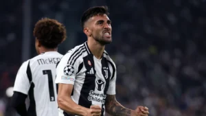 Juventus player Nico González celebrates passionately during a UEFA Champions League match, wearing the club’s black and white striped home kit.