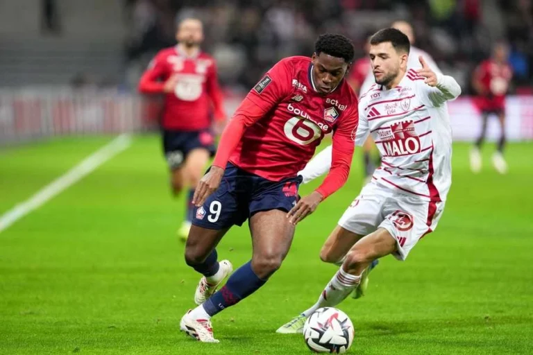Lille player in red battles for the ball against a Brest defender during a Ligue 1 match.