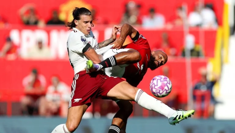 Arsenal defender Riccardo Calafiori in a white jersey challenges an opponent in a red jersey during a fierce battle for the ball in a match.