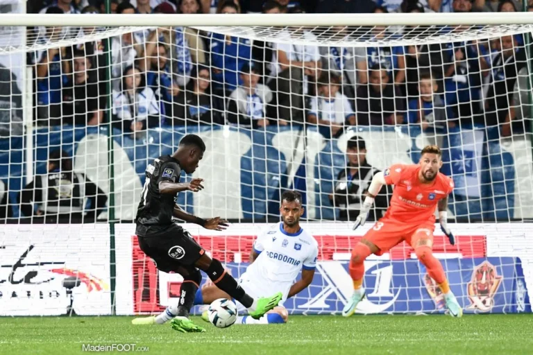 Dango Ouattara of FC Lorient prepares to shoot on goal against Auxerre, with a defender sliding and the goalkeeper ready to react.
